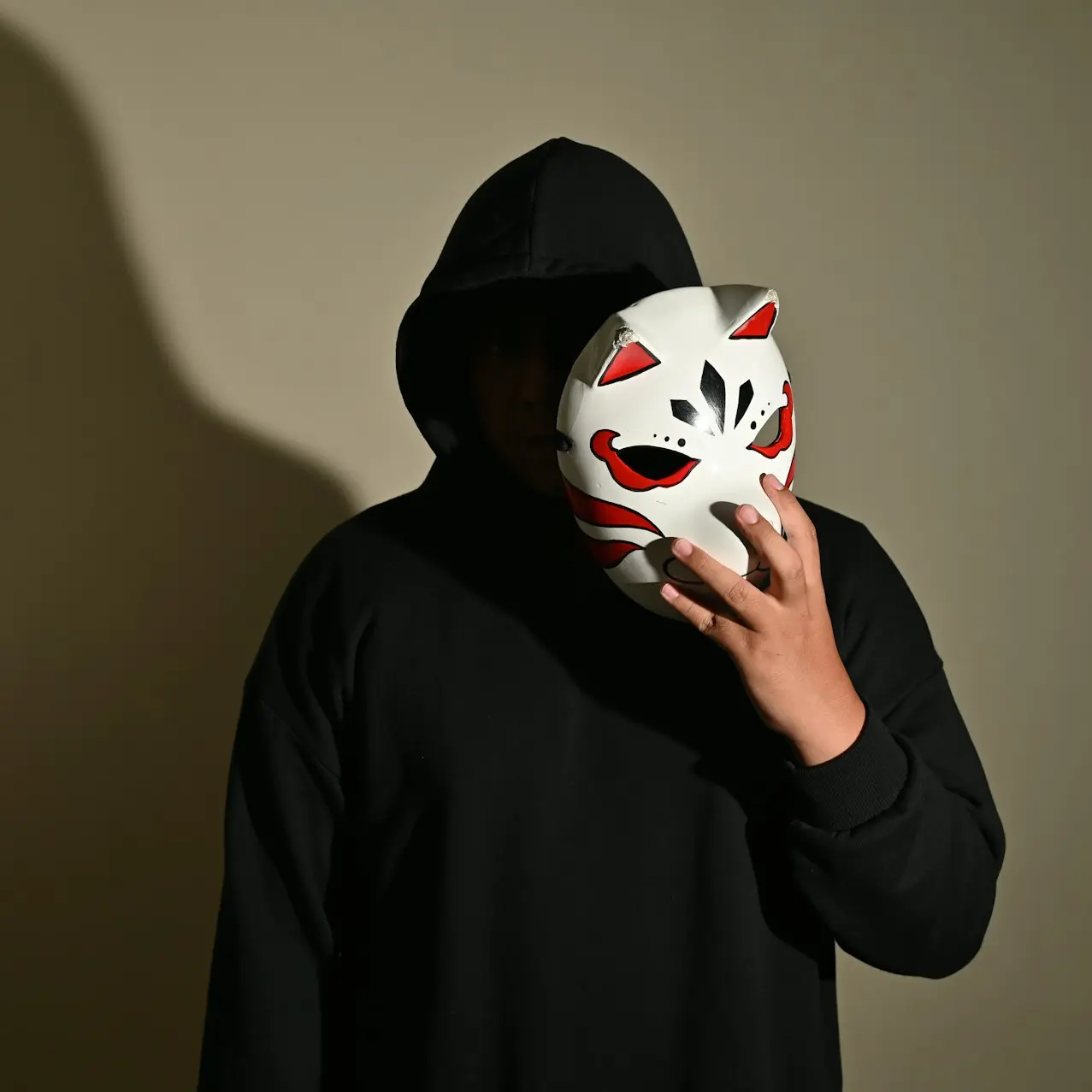 a man in a black hoodie holding a white mask